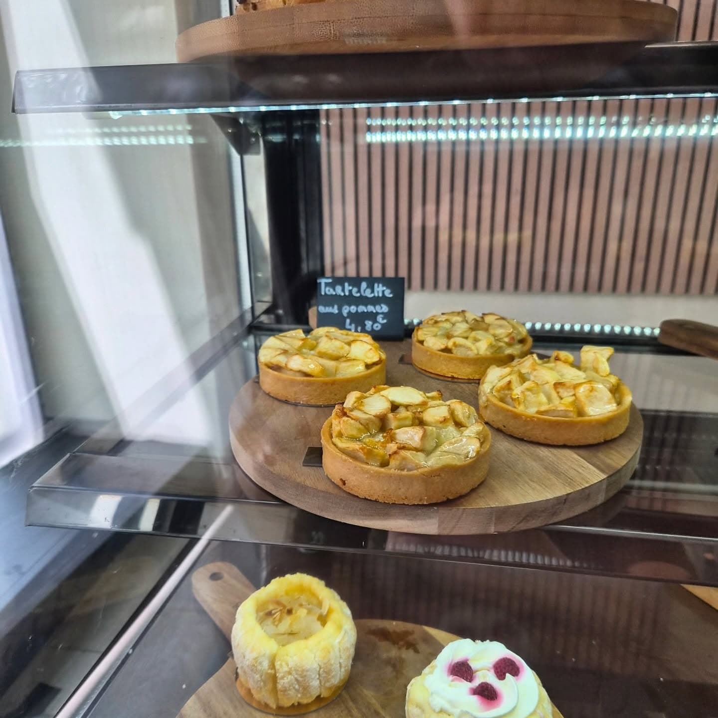 Quatre tartelettes aux pommes nappées, en morceaux dorés, sur une planche ronde