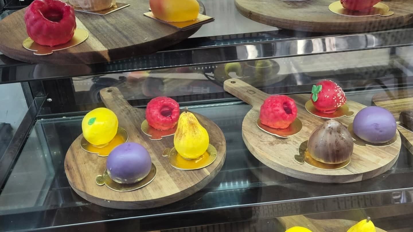 Les plateaux de bois de la vitrine, couverts d’entremets trompe-l’œil en forme de fruits